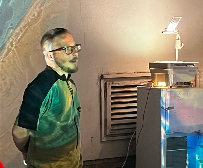 Balázs egy analóg írásvetítő mellett, színes fénnyel megvilágítva.
